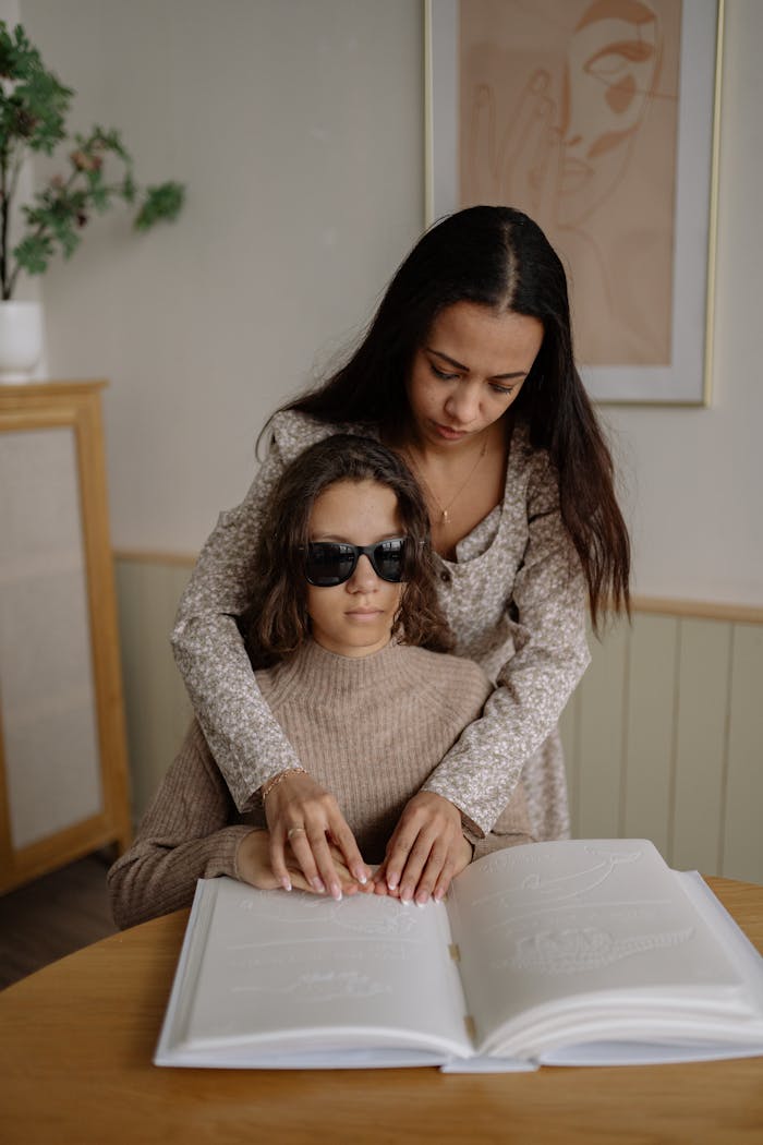 hero-img-01 A mother assisting her blind daughter with reading braille at home.